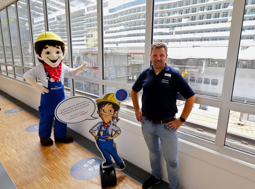 Maskottchen Kalle Kreuzer und Thorsten Eden, Leiter Guest Experience, an einer der verschiedenen Stationen: Die Panoramagalerie mit dem Blick auf die aktuell im Bau befindliche „Arvia“ für P&O Cruises. Foto: © Papenburg Marketing GmbH