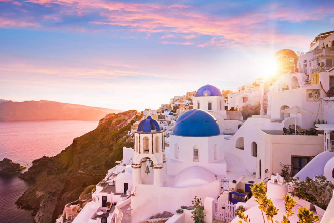 Blick bei Sonnenuntergang auf die blauen Kuppelkirchen von Santorin, Griechenland. Foto: © Adobe Stock / Lukas Gojda