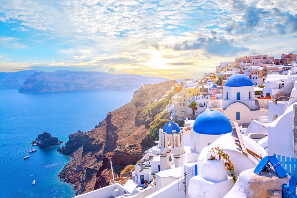 Die wunderschöne Stadt Oia auf der griechischen Insel Santorin. Traditionelle weiße Architektur und griechisch-orthodoxe Kirchen mit blauen Kuppeln über der Caldera, Ägäisches Meer. Malerischer Reisehintergrund.